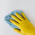 crop unrecognizable person in yellow gloves cleaning white surface