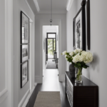 An image showcasing a narrow hallway in a small house adorned with a symmetrical arrangement of framed black-and-white photographs capturing serene landscapes, complemented by a sleek, minimalist console table with a vase of fresh flowers