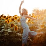 close up photography of woman dancing beside sunflower field during golden hour